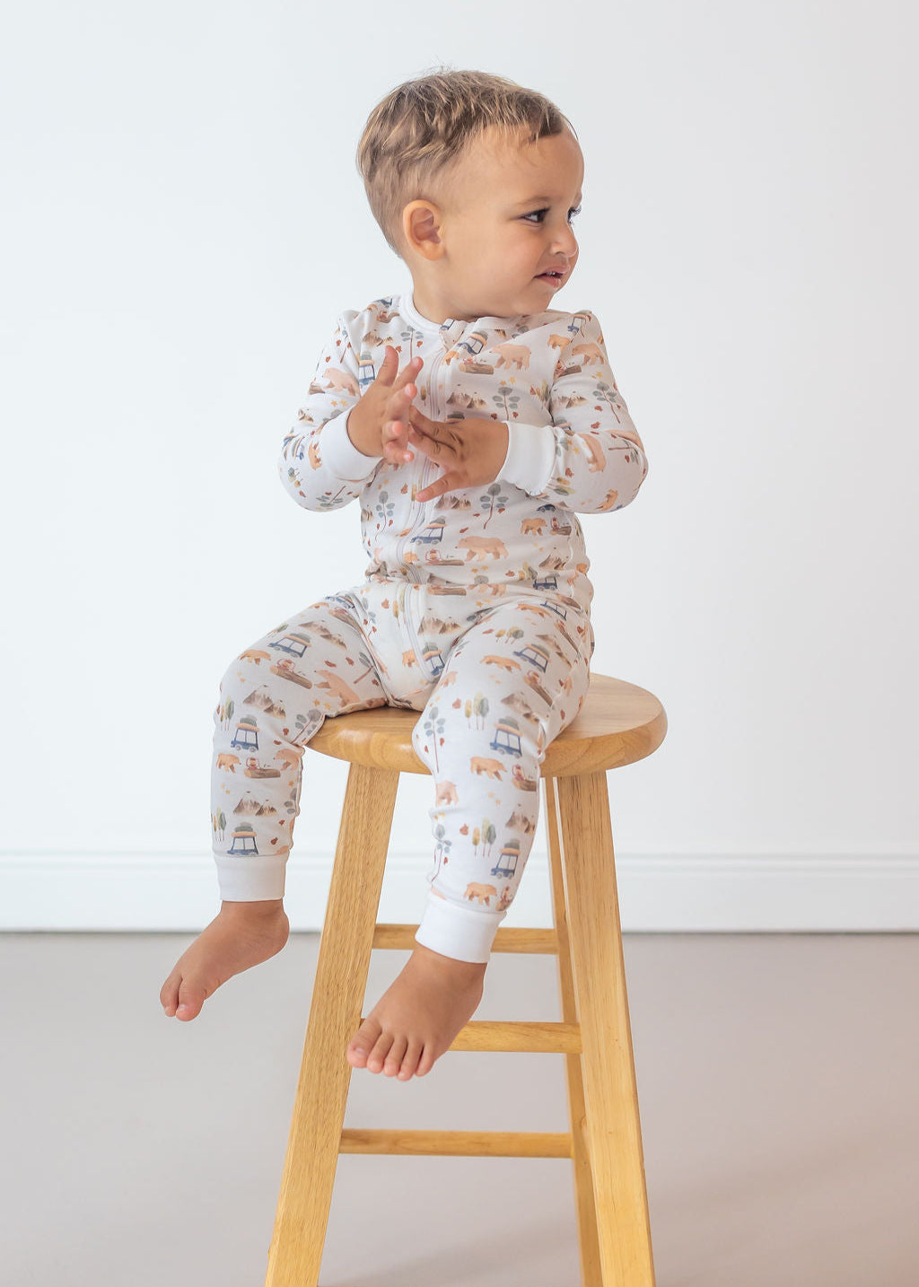 Child sitting on a wooden stool wearing a patterned onesie against a white background