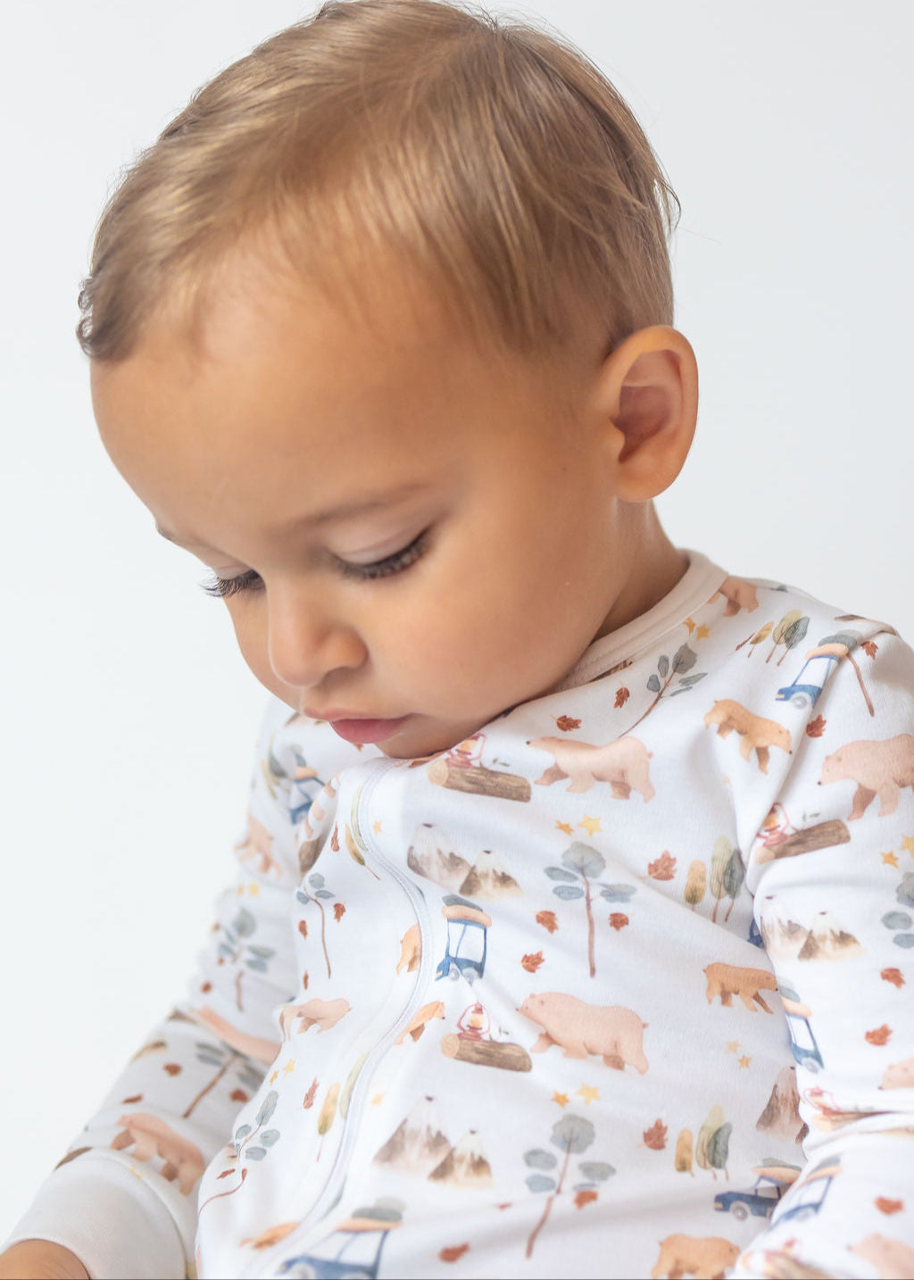 Child wearing a patterned onesie with farm animals on a plain background