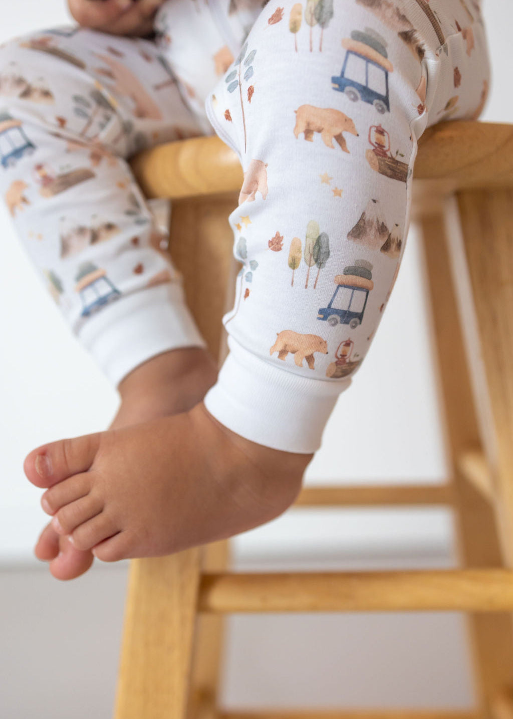 Child wearing patterned leggings with animals and vehicles on a wooden stool.
