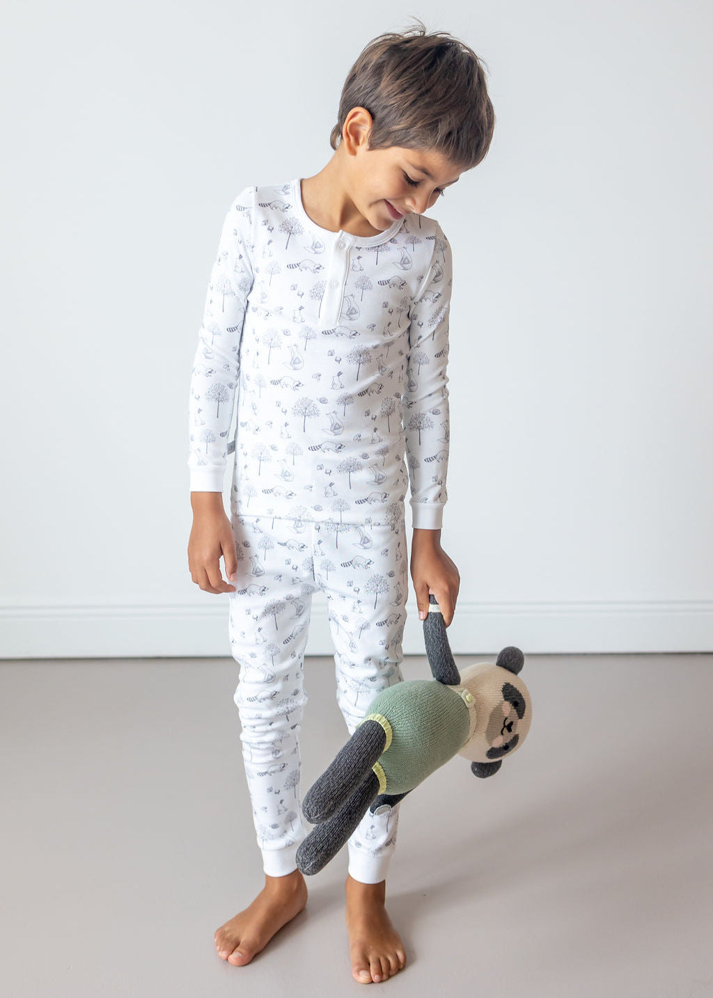 Child wearing a white pajama set with gray patterns, holding a green teddy bear.