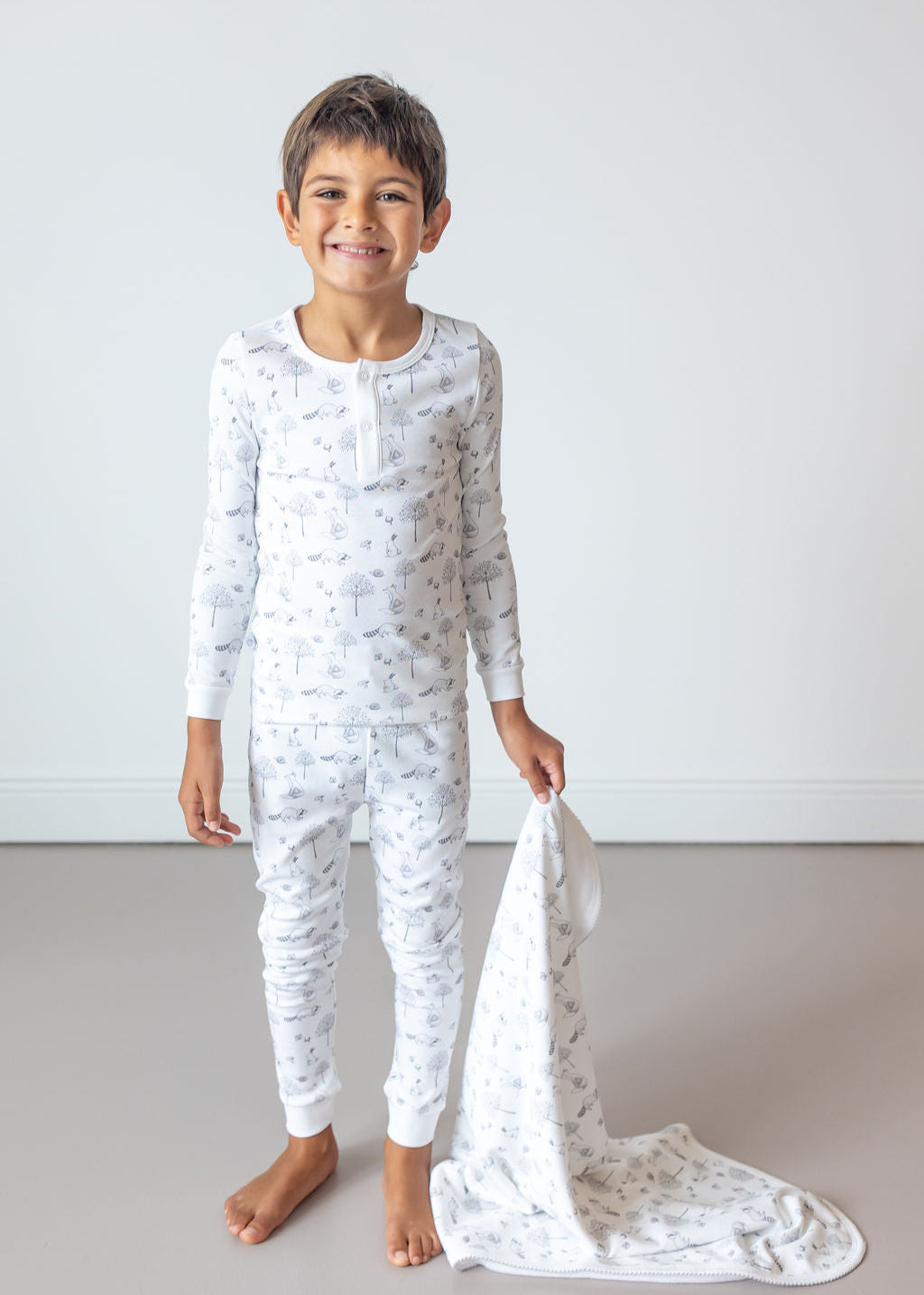 Child wearing a white pajama set with a subtle pattern, holding a matching blanket.