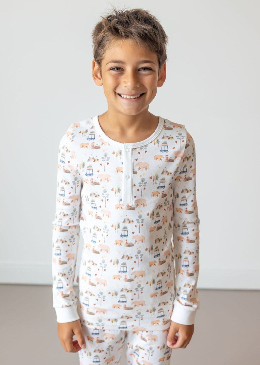 Child wearing a long-sleeve pajama set with vehicle pattern on a plain background