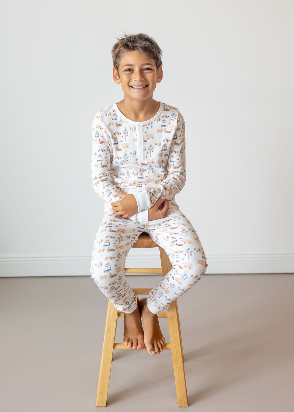 Child wearing a floral pajama set sitting on a wooden stool against a plain background