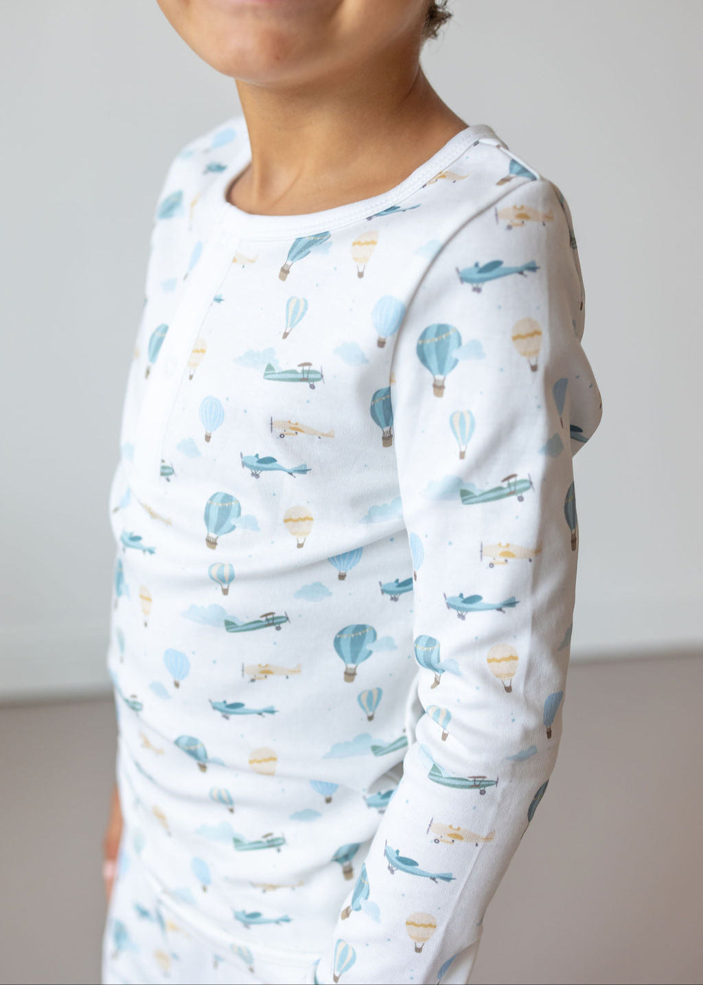 Child wearing a long-sleeve shirt with airplane pattern against a plain background