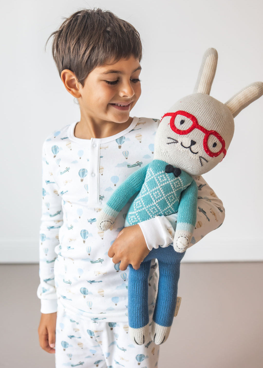 Child holding a plush toy with glasses against a plain background