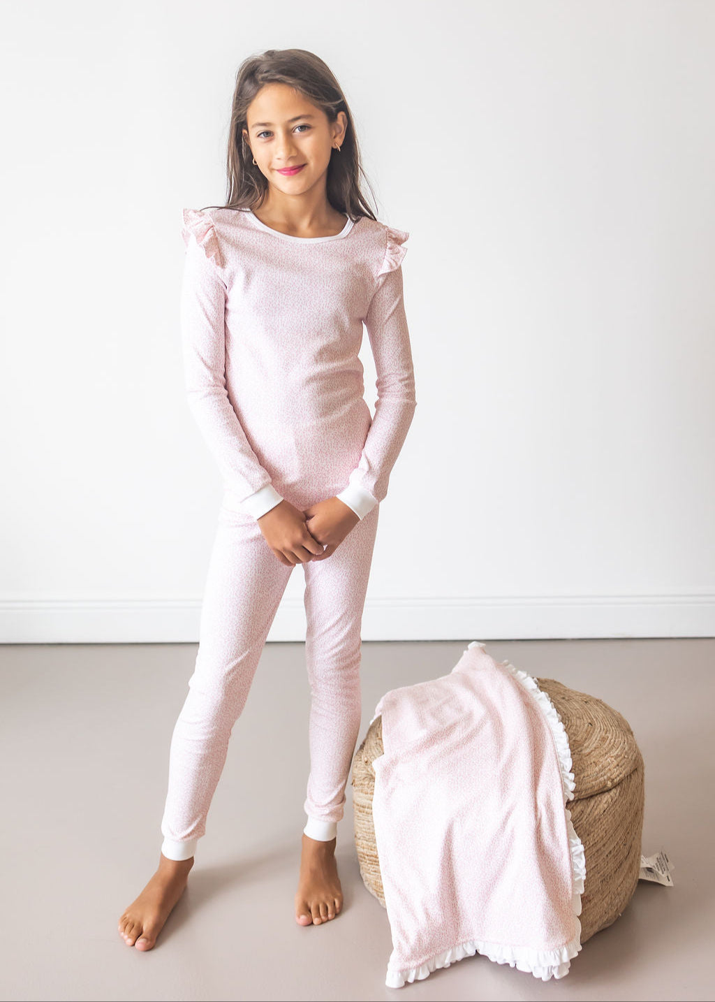 Young girl wearing a pink pajama set with ruffled details, standing against a white background.