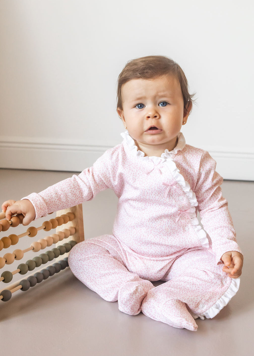 Baby in a pink outfit sitting on a light-colored floor with an abacus.