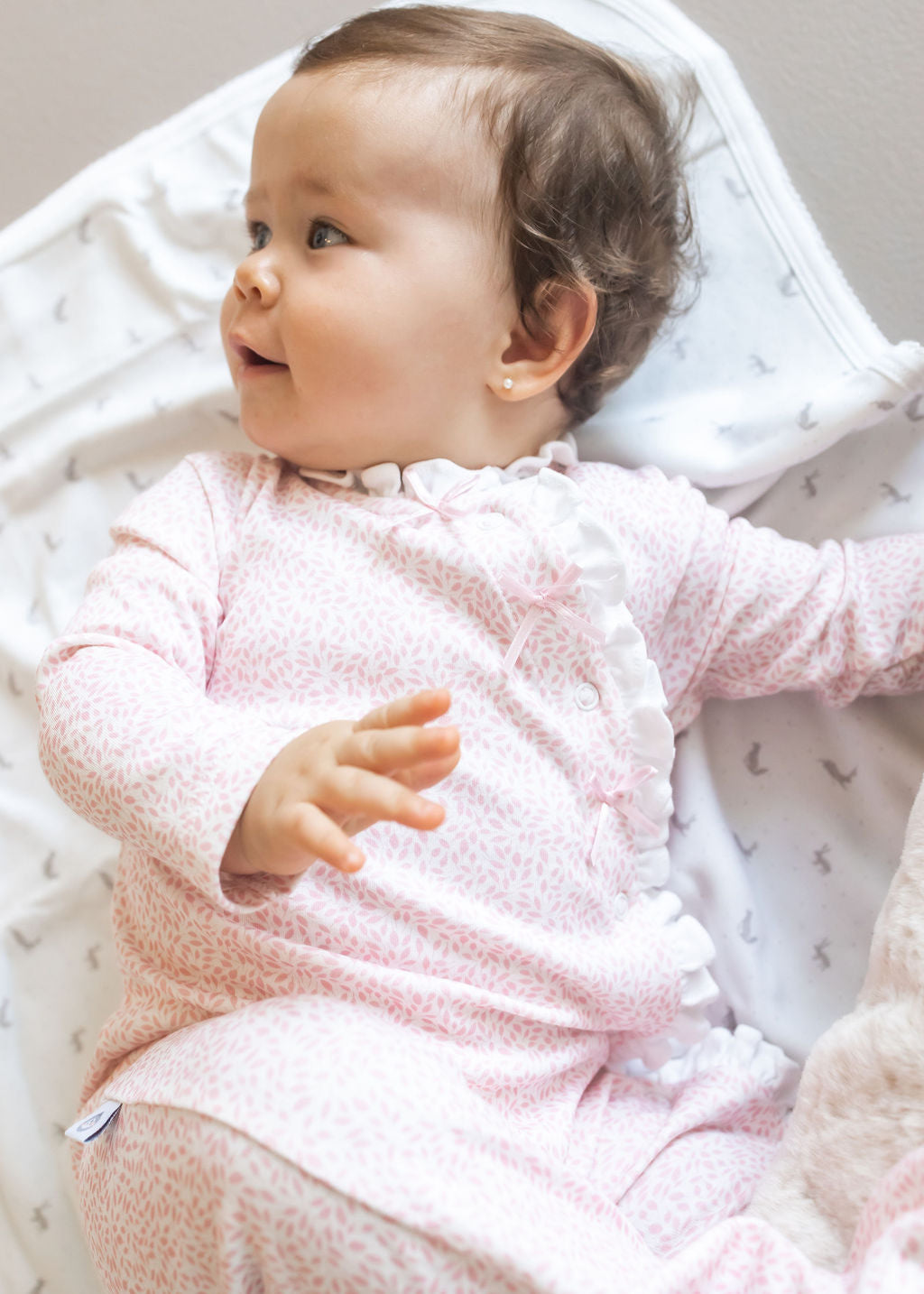 Baby in a pink outfit lying on a white blanket