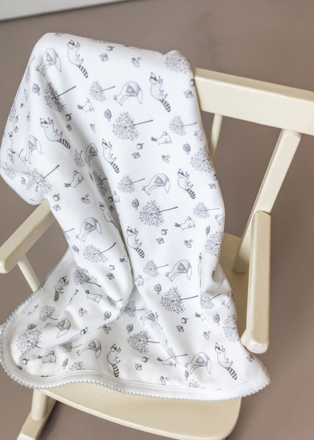 White baby blanket with black patterns draped over a wooden chair.