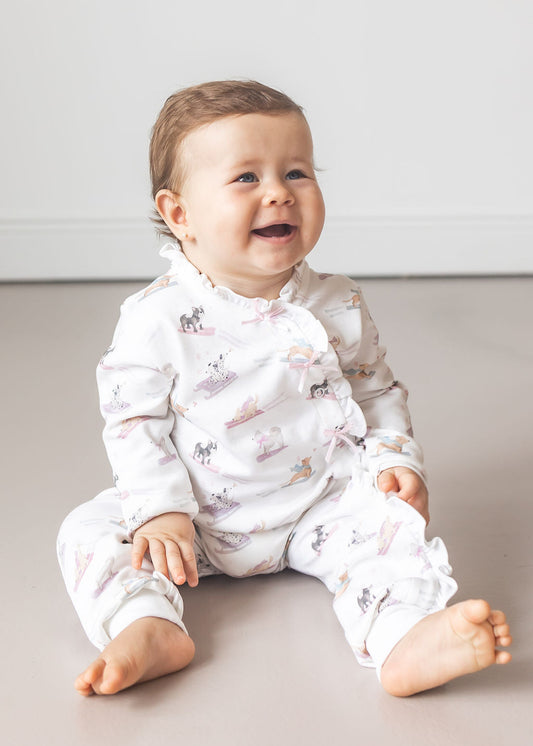 Baby wearing a white onesie with animal prints sitting on a light gray floor.