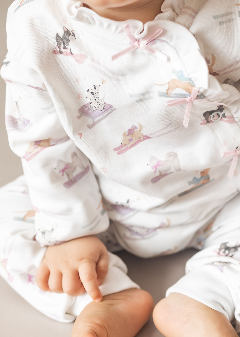Baby wearing a white outfit with pink bows and animal prints on a light background