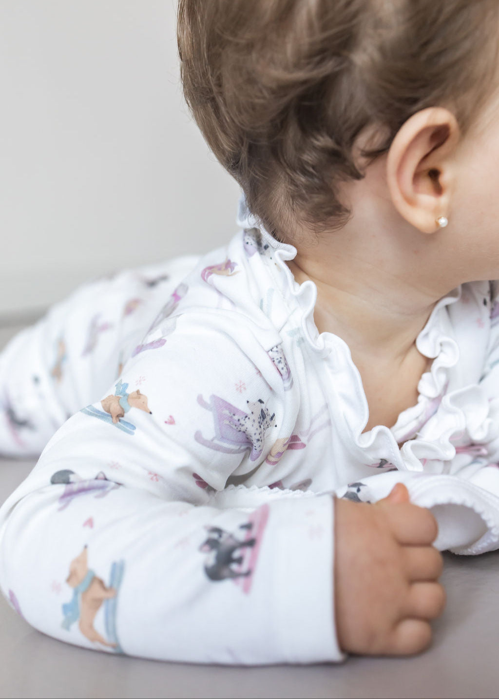 Baby wearing a white outfit with colorful patterns on a neutral background