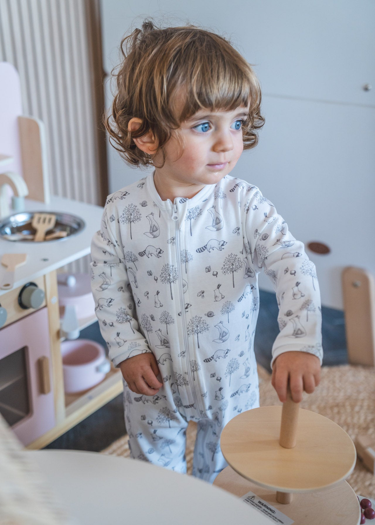 Child playing with a wooden toy in a room with a white wall and furniture.
