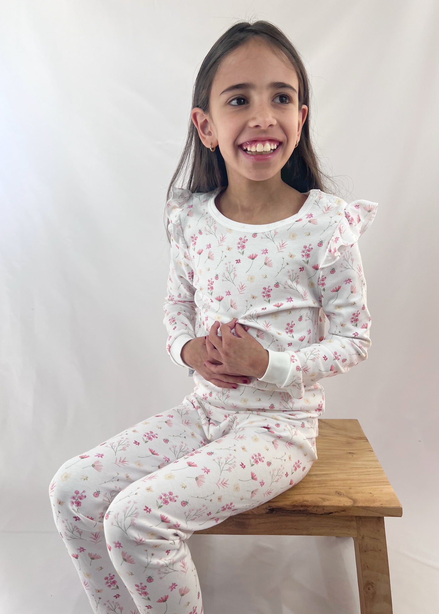 Young girl wearing a floral pajama set sitting on a wooden stool against a white background
