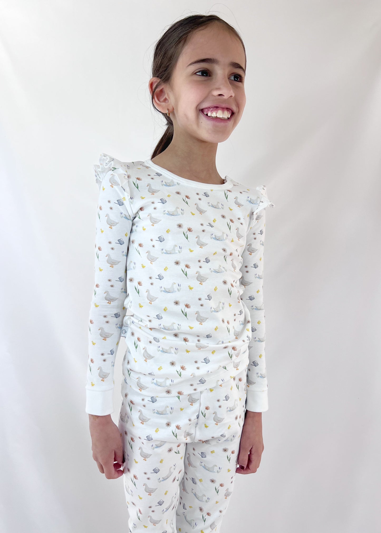 Young girl wearing a white long-sleeve top and pants with a subtle pattern on a plain background