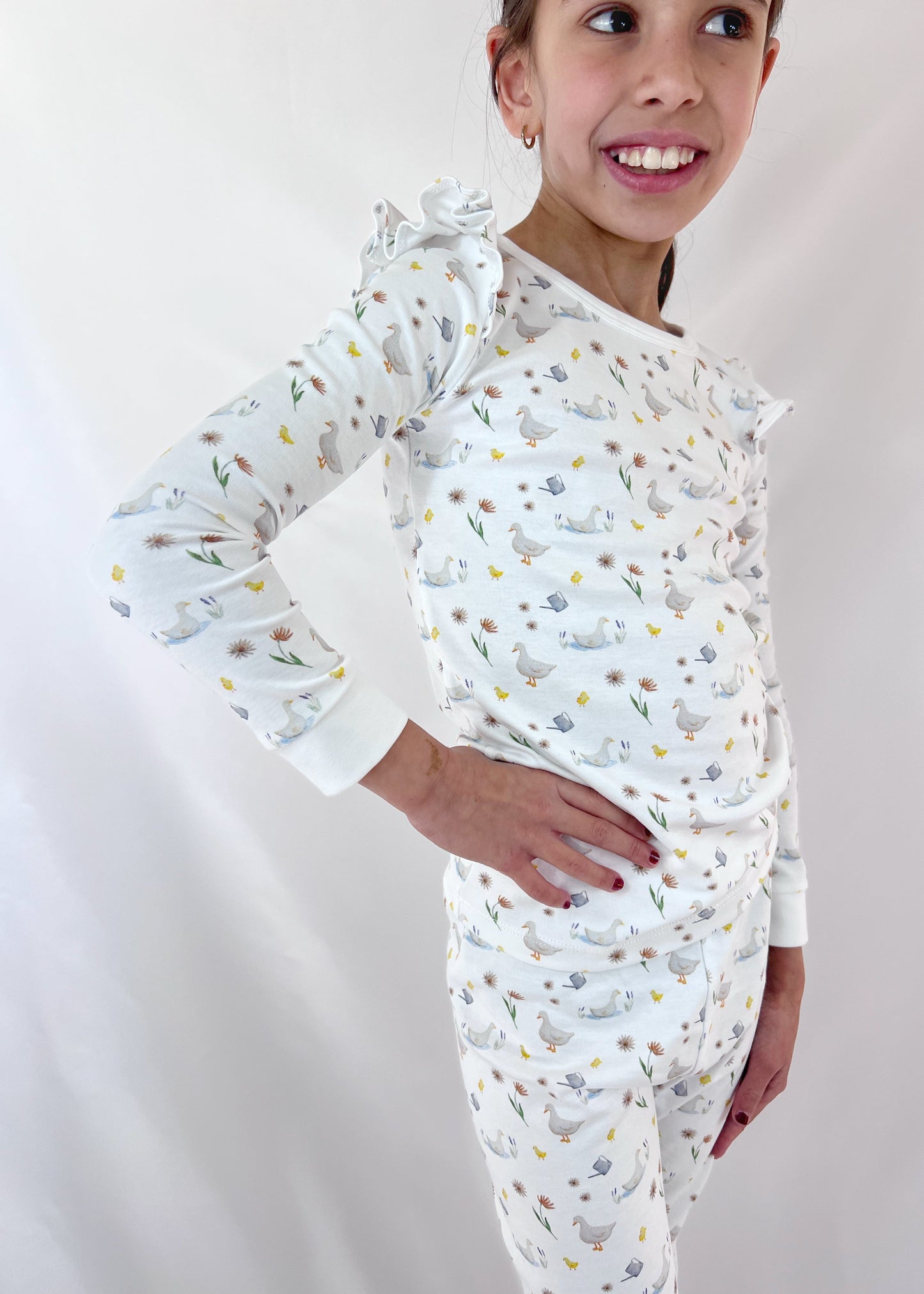 Child wearing a white long-sleeve shirt and pants with animal pattern on a plain background