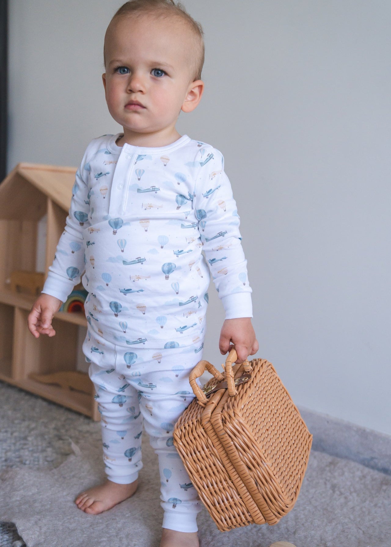 Baby in light blue pajamas holding a woven basket indoors.