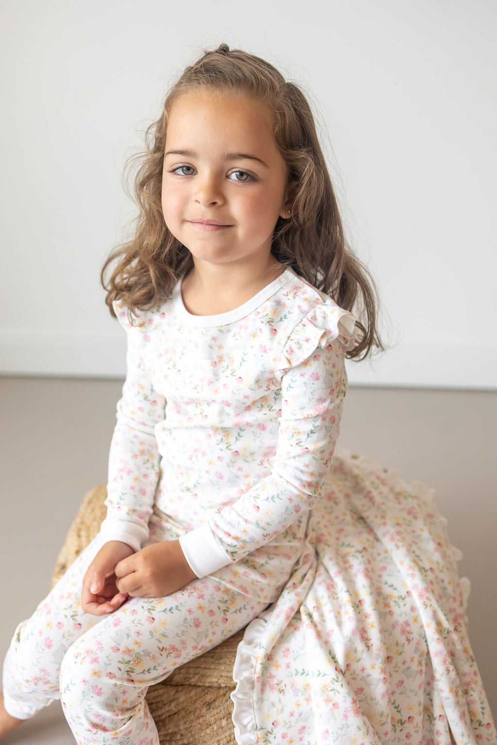 Young girl wearing a floral dress sitting on a chair against a plain background