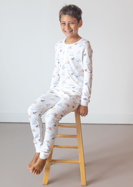 Child wearing a white pajama set with a pattern, sitting on a wooden stool against a plain background.