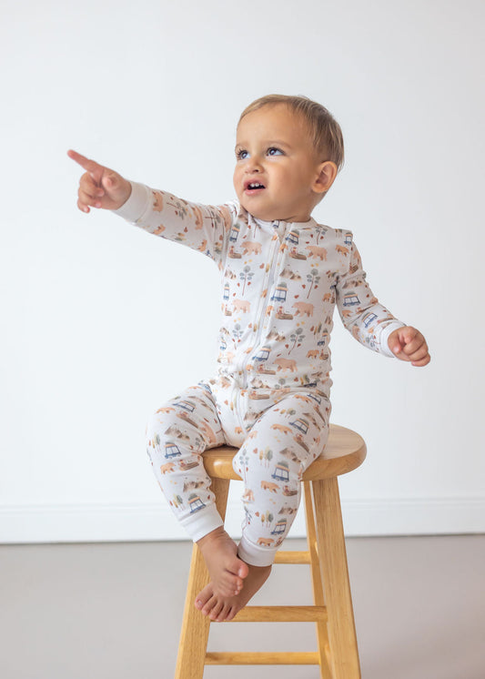 Baby in a patterned onesie sitting on a wooden stool against a white background