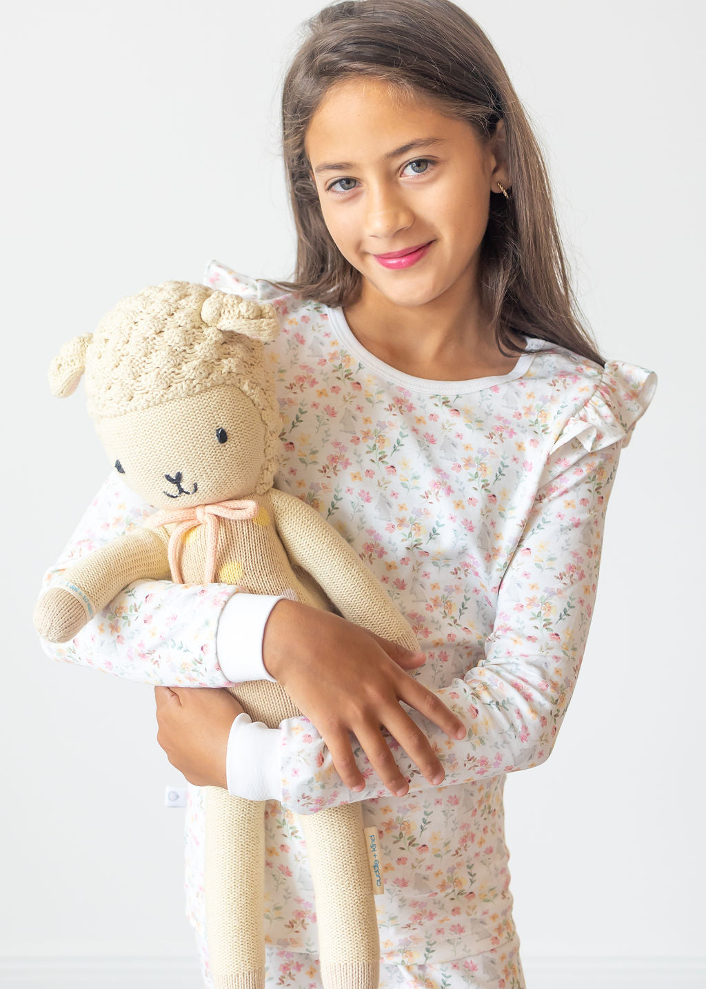 Young girl holding a plush sheep toy against a white background