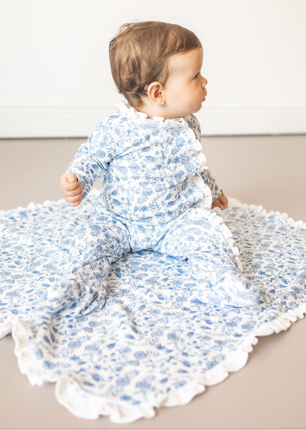 Baby in a floral outfit sitting on a textured blanket