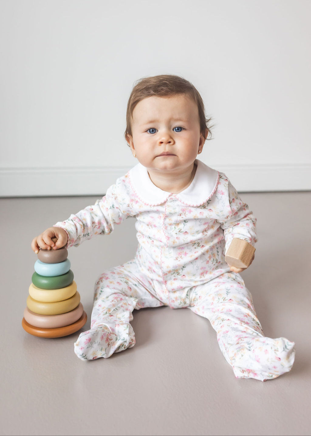 Baby sitting on a light-colored floor with a colorful stacking toy