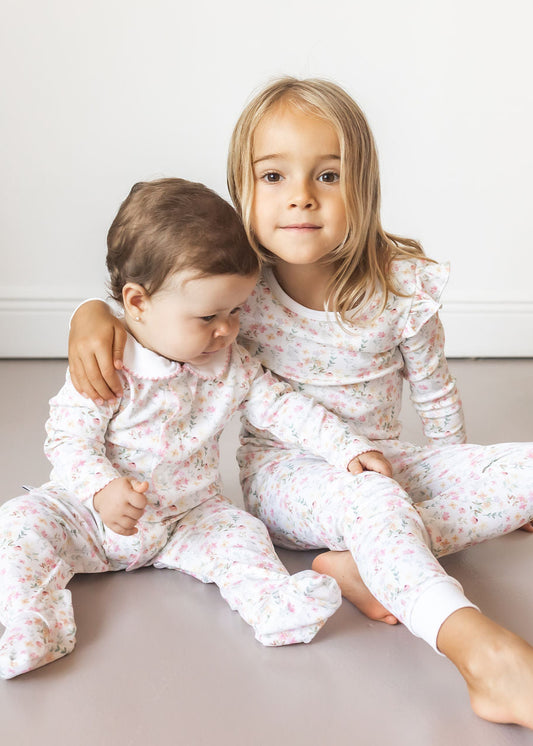 Two children in matching floral pajamas sitting on a light-colored floor.