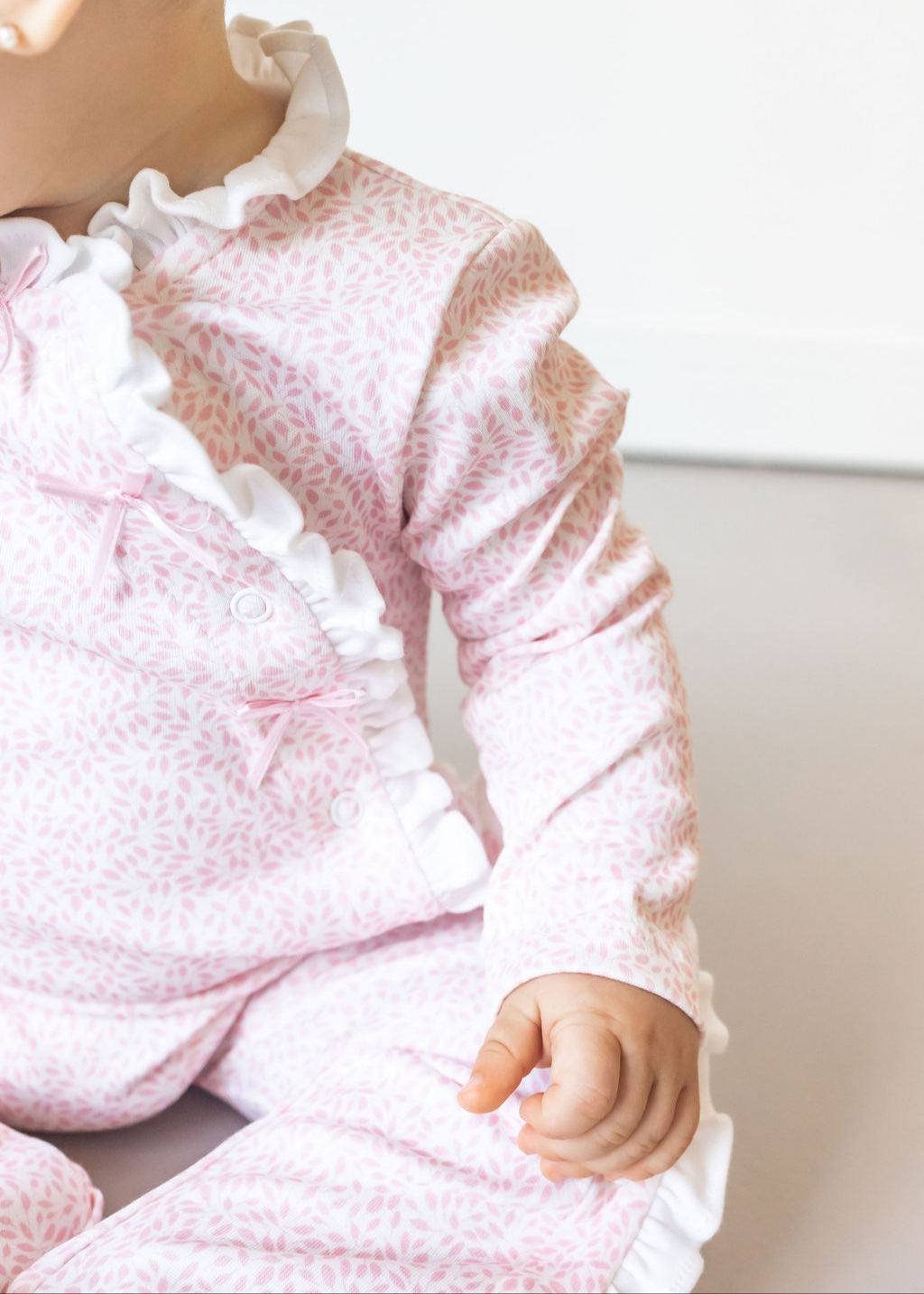 Close-up of a baby wearing a pink textured outfit with white ruffles on a light background