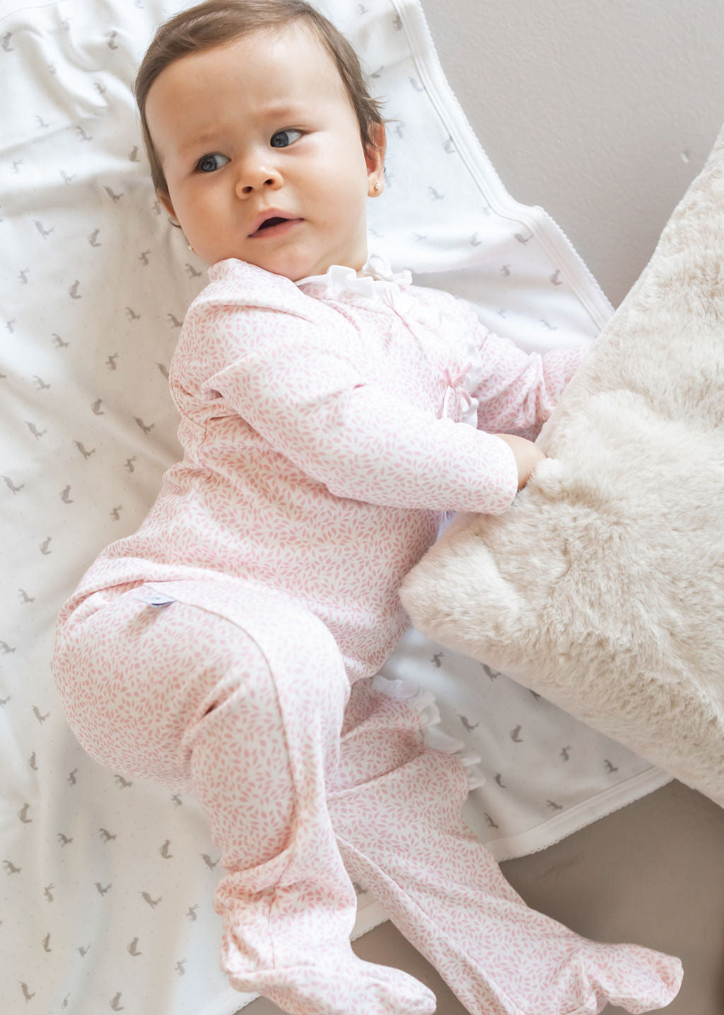 Baby in pink outfit lying on a textured blanket