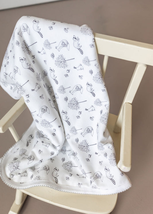 White baby blanket with black patterns draped over a wooden chair.