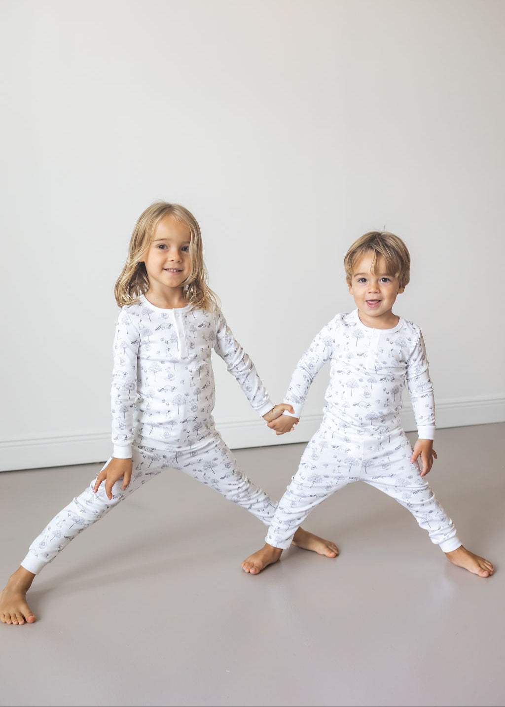 Two children wearing white pajamas with black patterns on a plain background