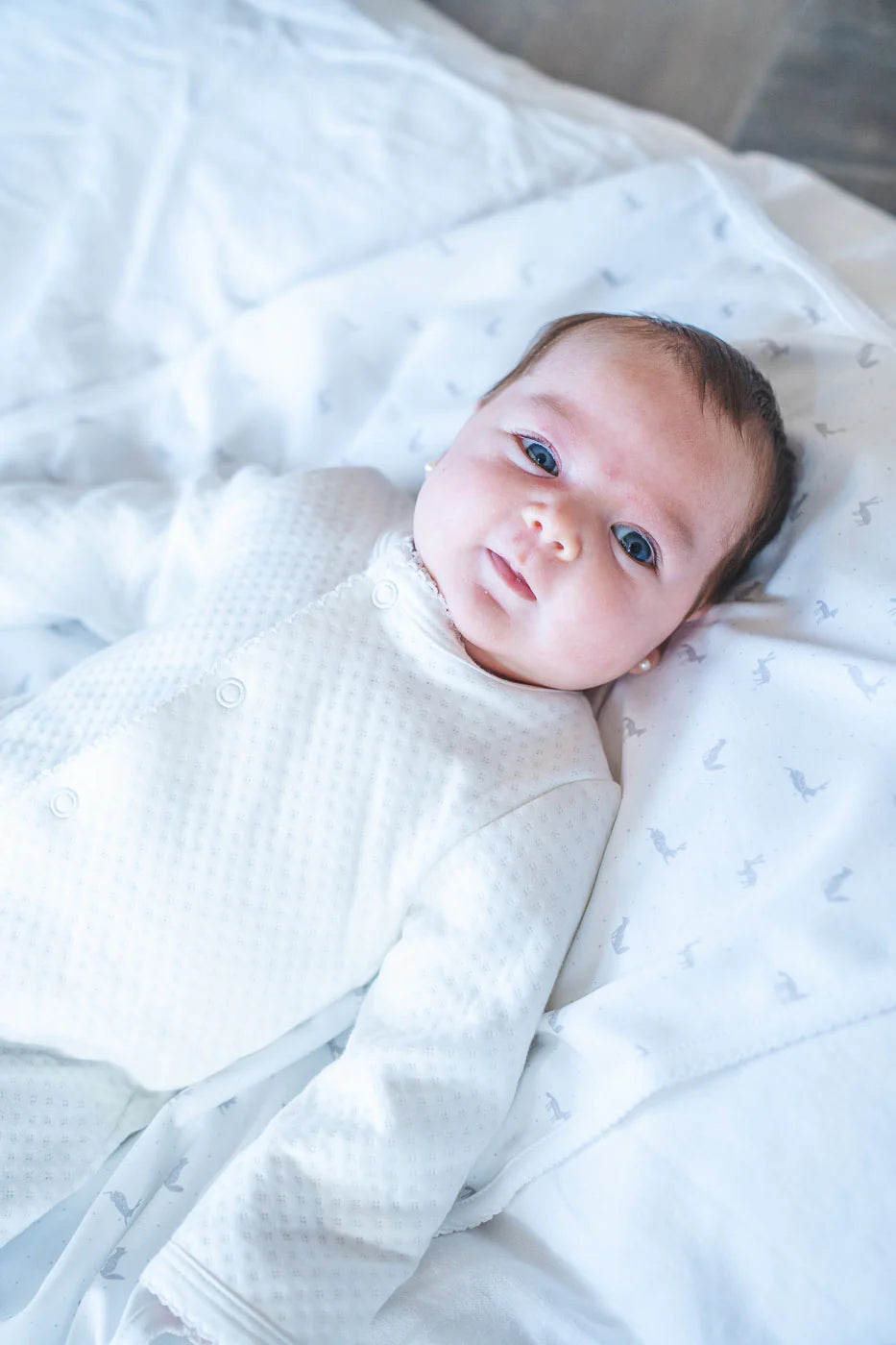 Newborn baby wrapped in a white blanket on a soft surface