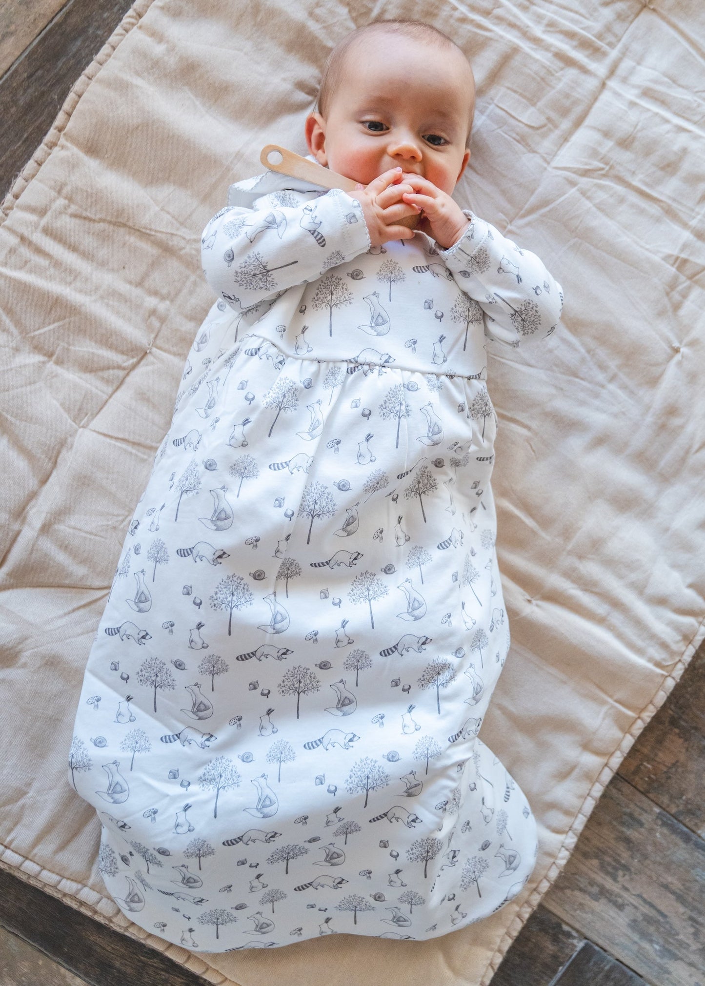 Baby wrapped in a white swaddle with gray patterns on a beige quilted blanket.