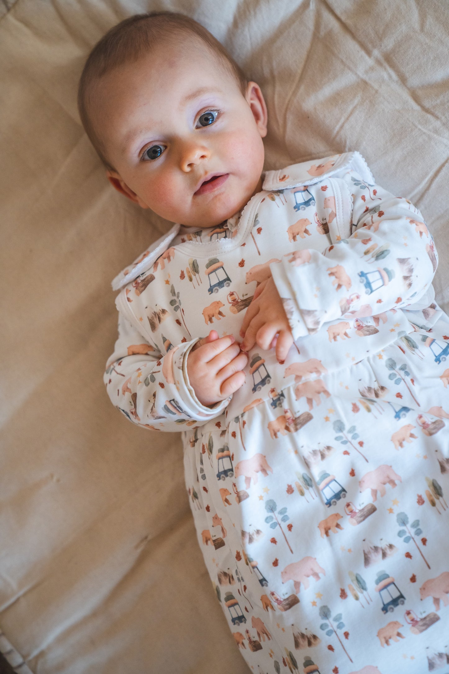 Baby lying on a beige blanket wearing a patterned onesie.