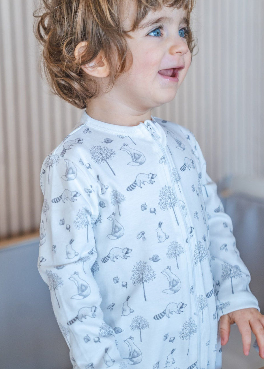 Child standing in a crib wearing a light blue long-sleeve shirt with a floral pattern.
