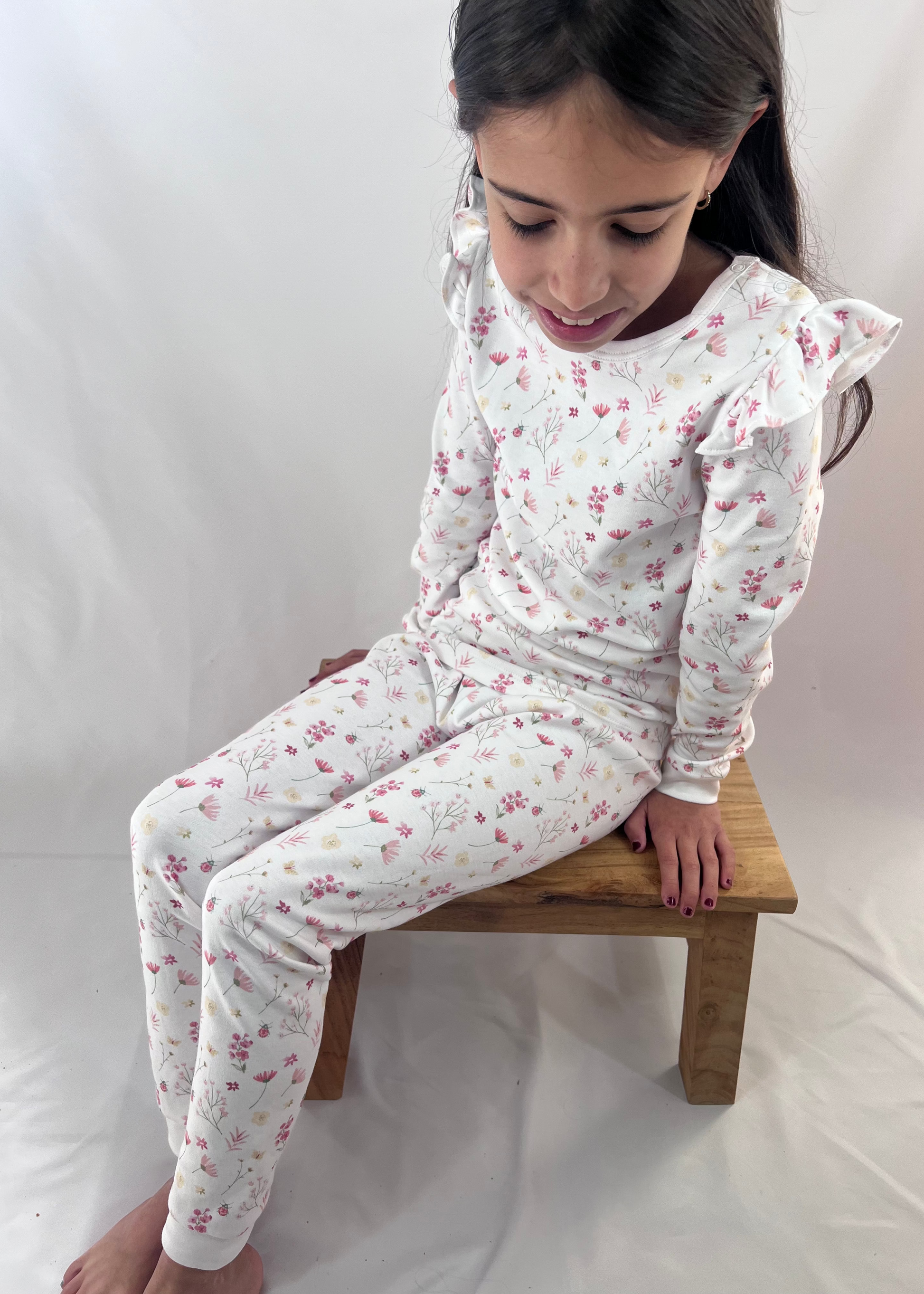 Young girl wearing a floral pajama set sitting on a wooden stool against a white background