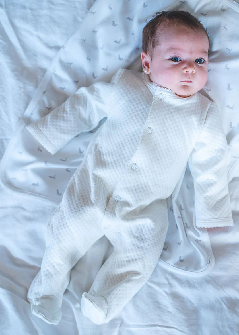 Newborn baby in a white outfit lying on a white blanket