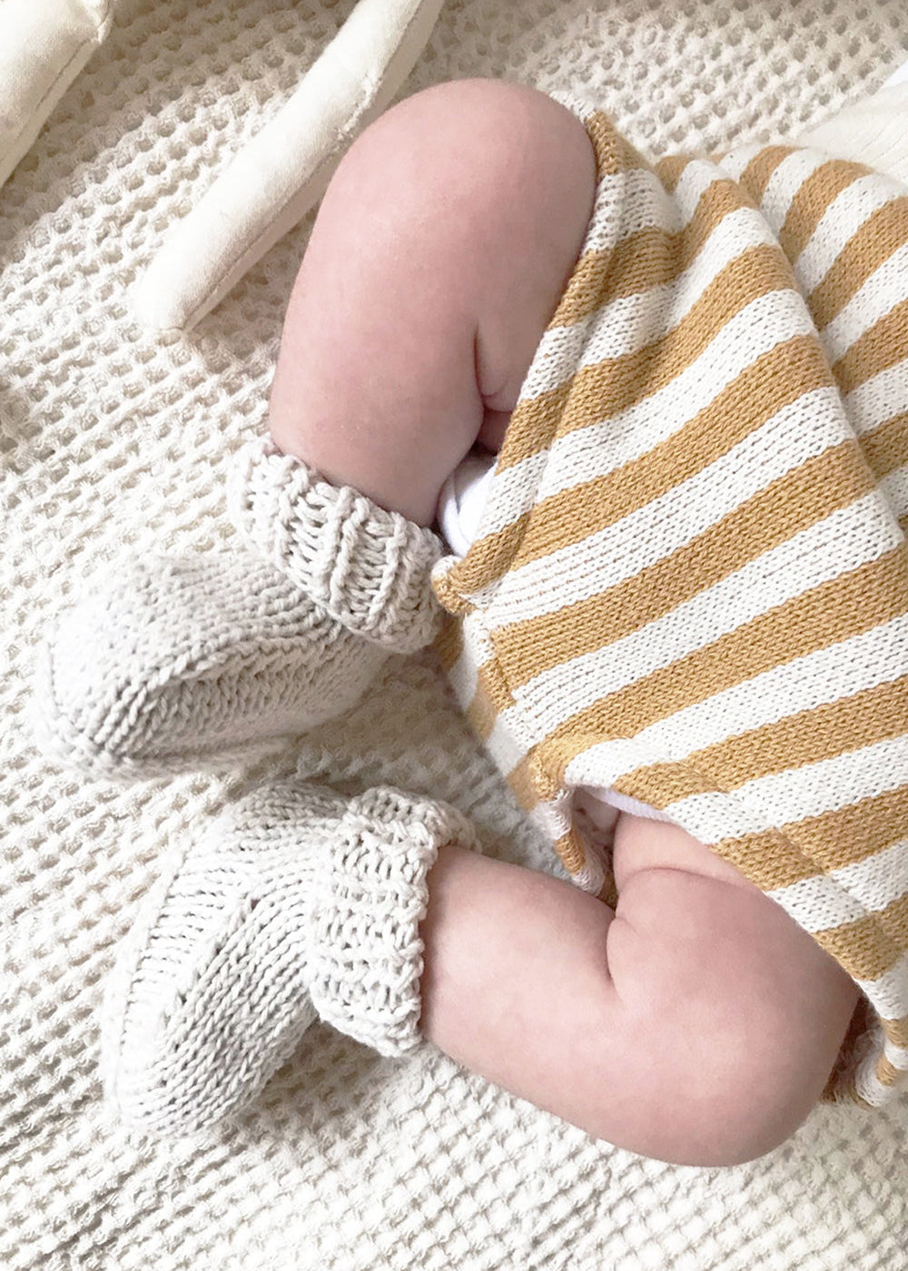 Close-up of a baby's legs wearing striped pants and white socks on a textured surface.