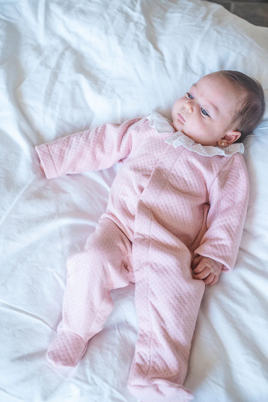 Baby in a pink onesie lying on a white blanket