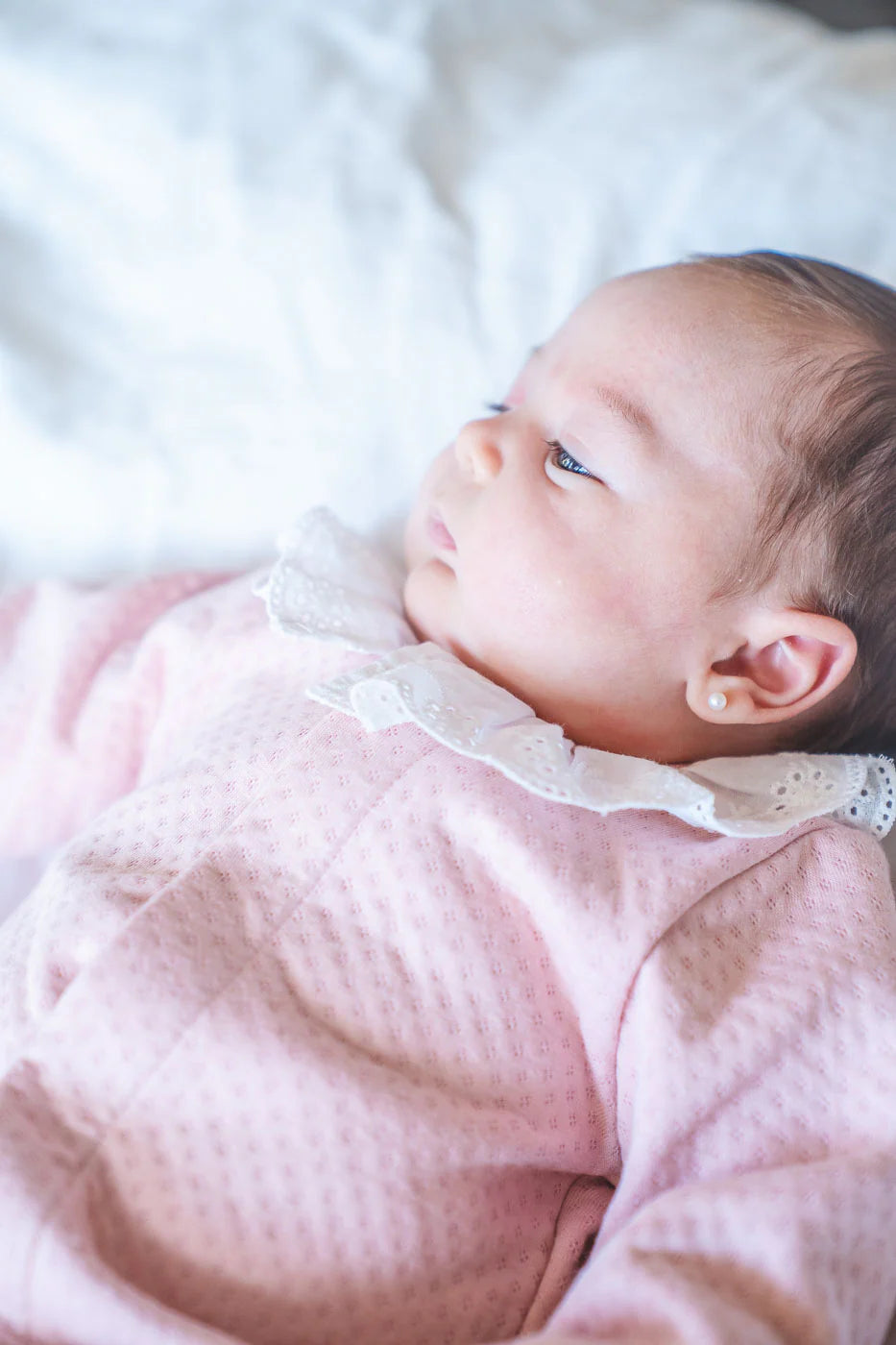 Baby in a pink outfit lying on a white blanket
