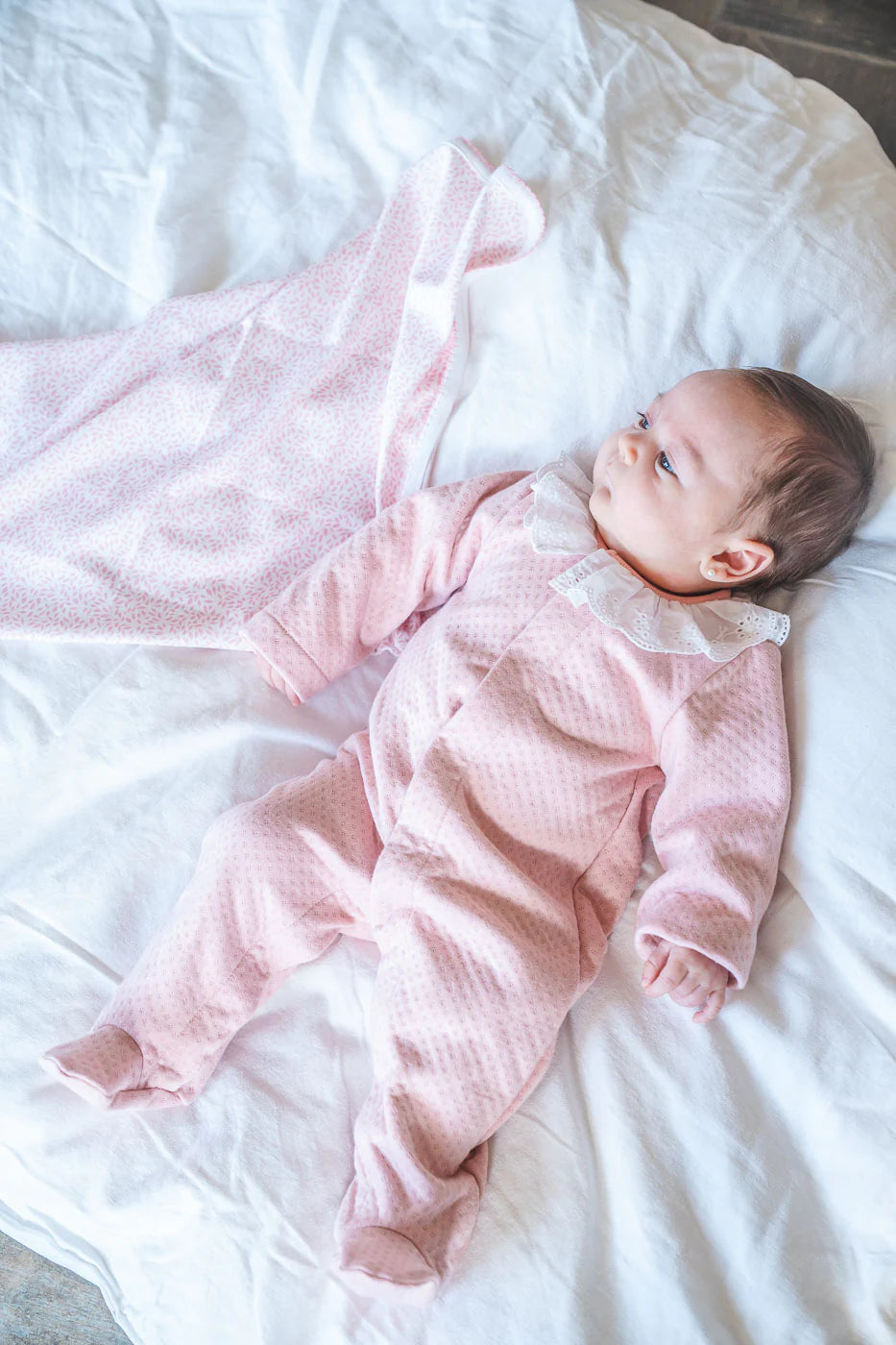 Baby in a pink outfit lying on a white blanket